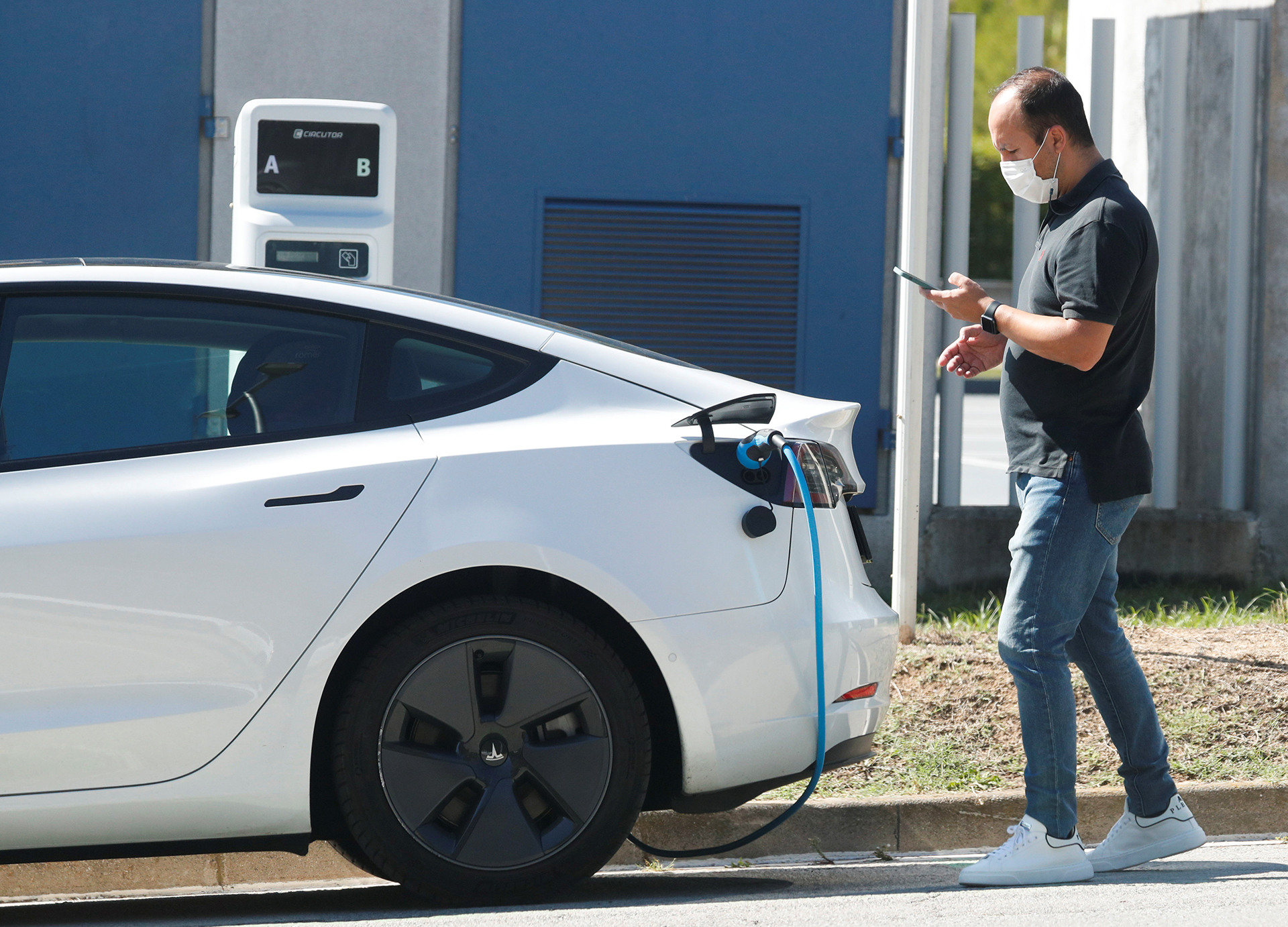 A man checks his mobile phone while he charges a Tesla electric car at a public charging point in Sant Cugat del Valles, near Barcelona, Spain, September 17, 2021. REUTERS/Albert Gea