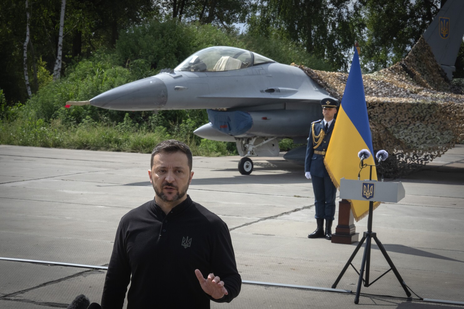 Ukraine's President Volodymyr Zelenskyy answers media questions standing against the background of Ukraine's Air Force's F-16 fighter jets in an undisclosed location in Ukraine, Sunday, Aug. 4, 2024. The F-16 fighter jets that have been delivered to Ukraine by Western countries will be flying sorties in Ukrainian skies and helping the country's current fleet of Soviet-era jets to counter Russia's invasion. (AP Photo/Efrem Lukatsky)