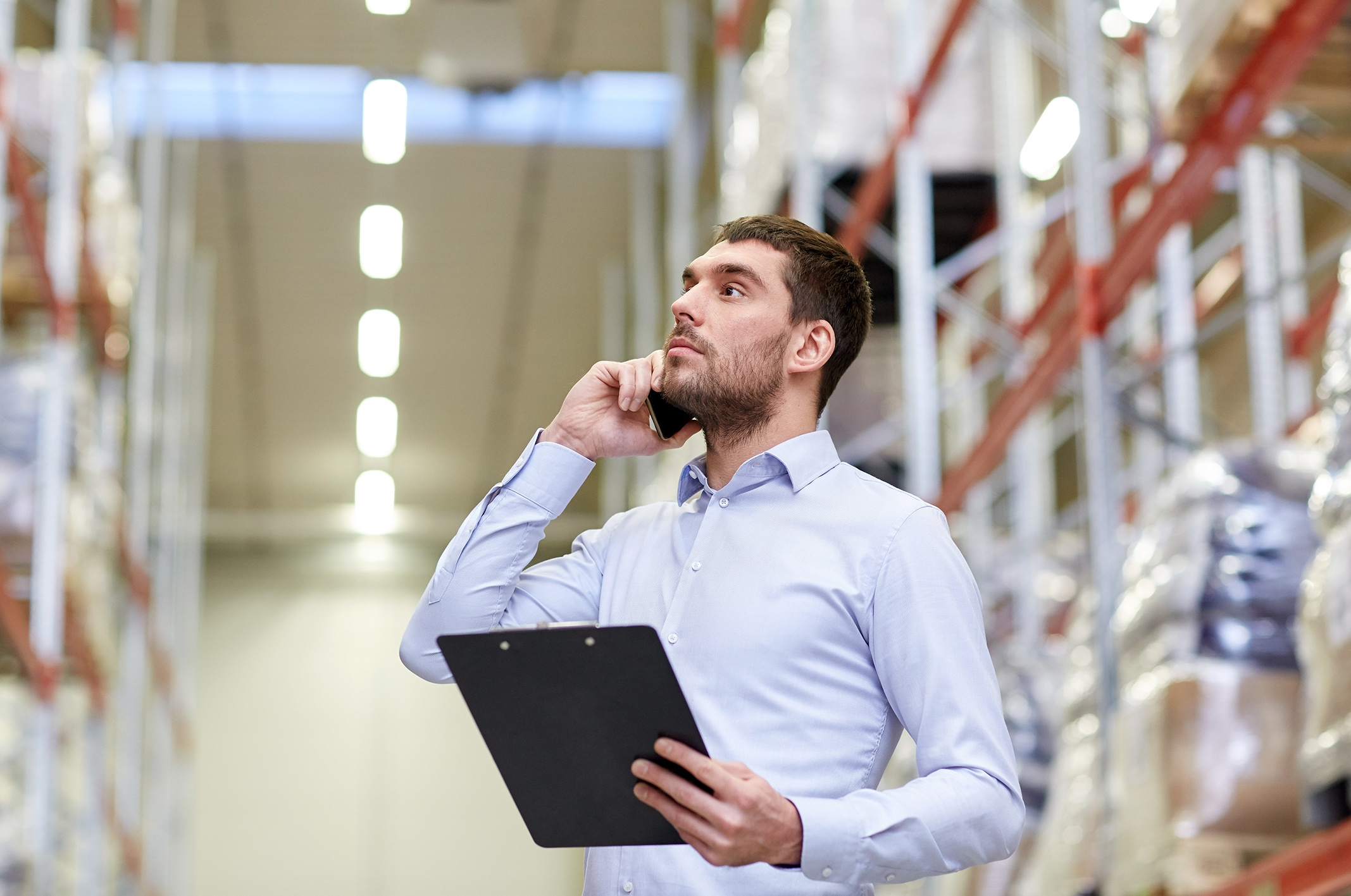 man with clipboard and smartphone at warehouse